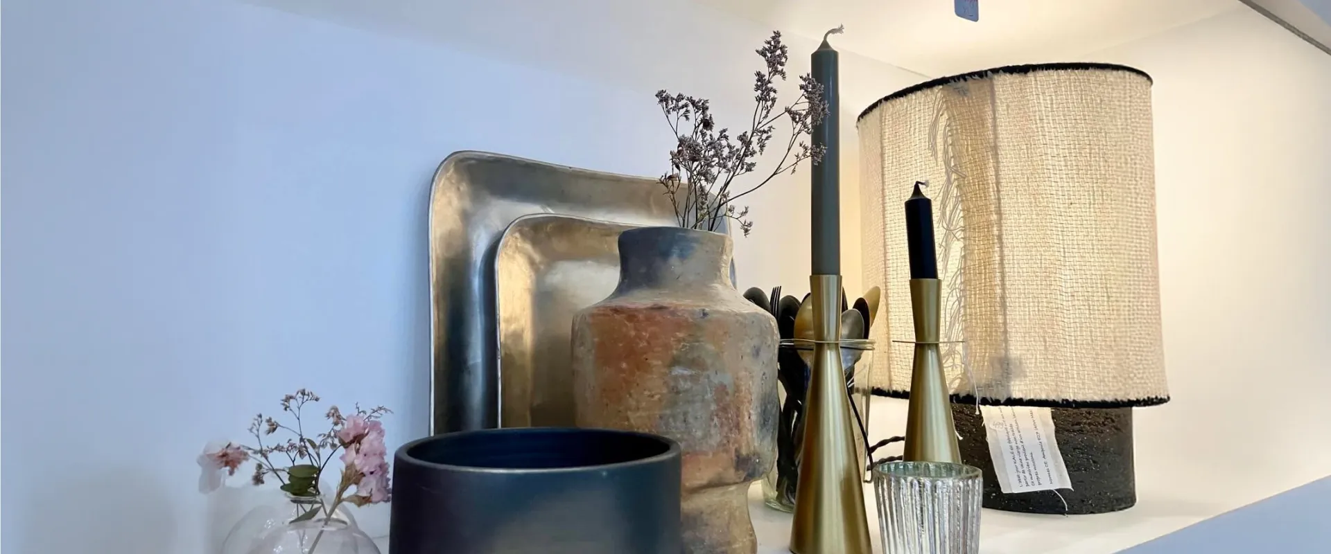 Une étagère de la boutique : vases, bougeoirs, lampe à abat-jour tressé et fleurs séchées