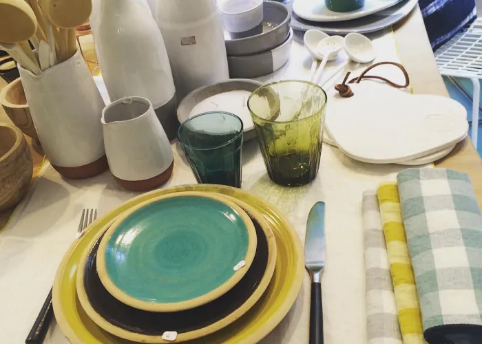 Table dressée : assiettes jaunes et vertes, verres colorés, pichets en céramique et serviettes vichy