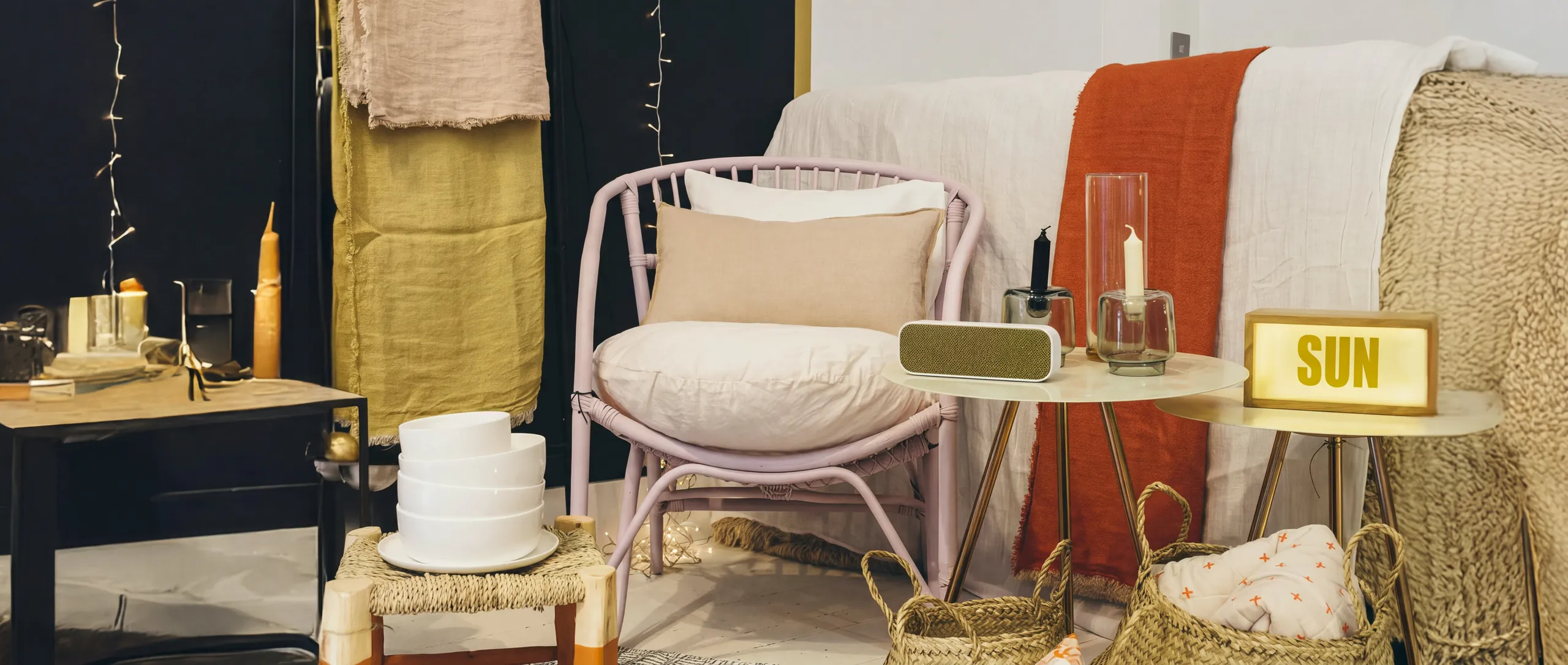 L'intérieur de la boutique : fauteuil rose, plaids ocre et rouille, bougies et paniers tressés