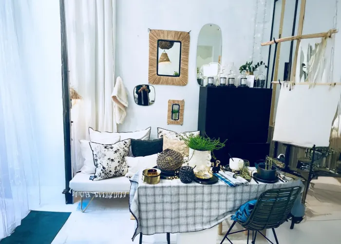 Un coin de la boutique : table nappée de carreaux, miroirs, fauteuil et coussins