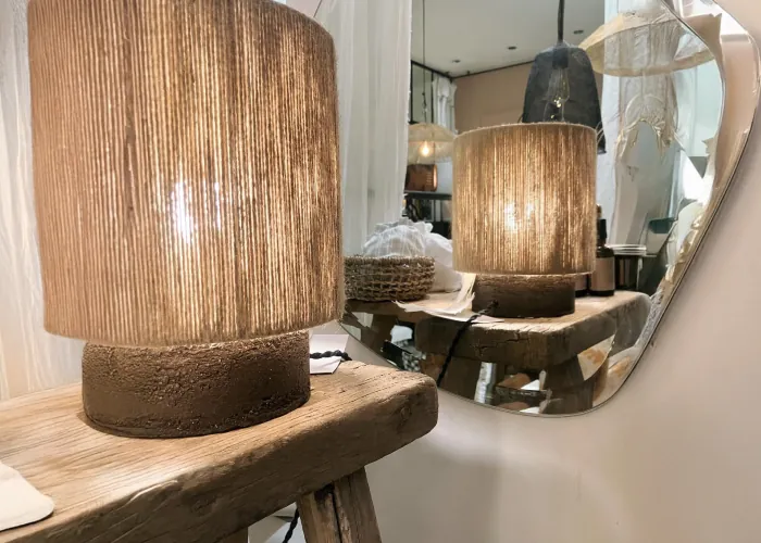 Lampe en jute allumée sur un banc en bois brut, reflétée dans un miroir
