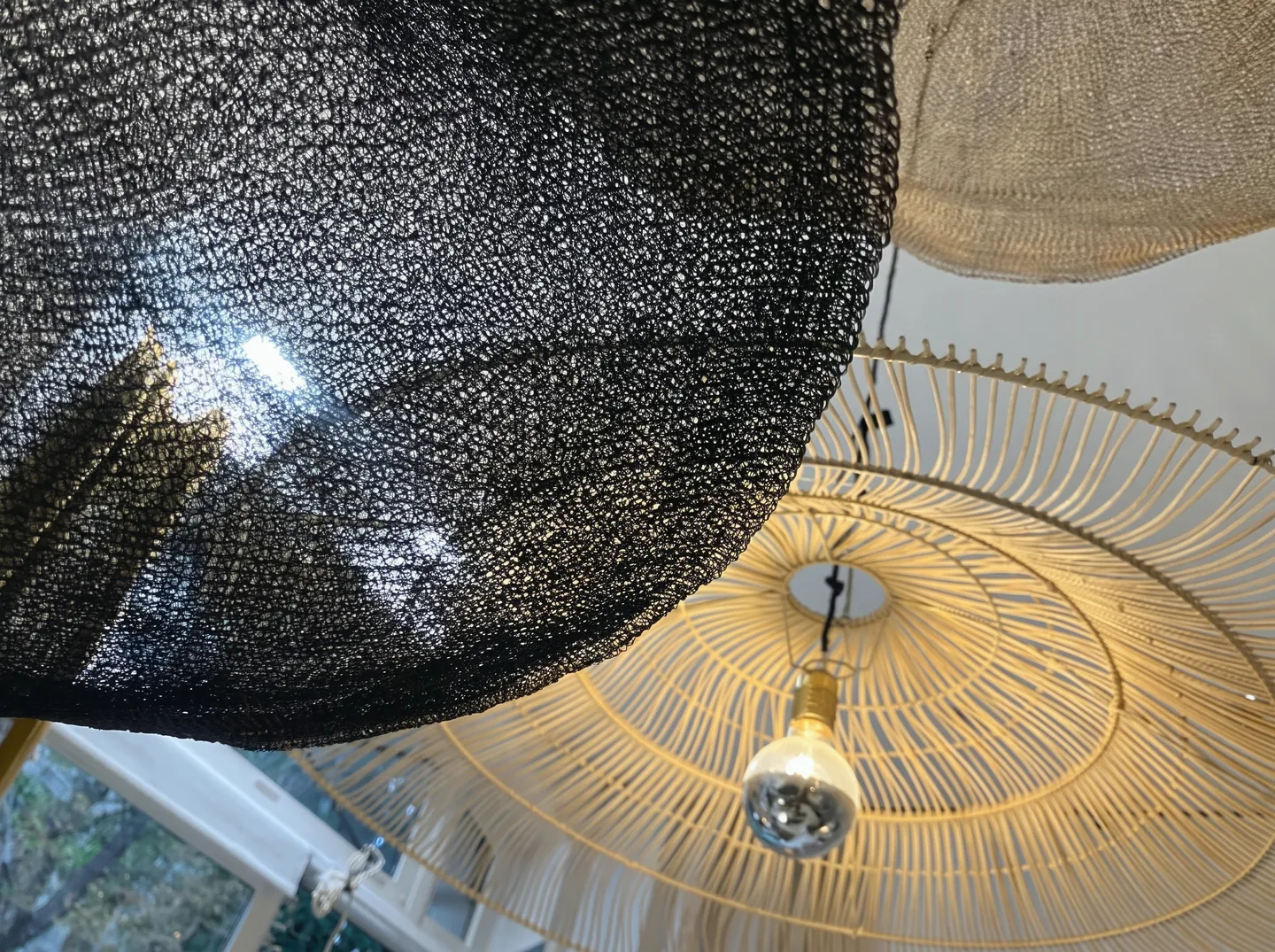 Suspensions vues d'en dessous : l'une en maille noire, l'autre en rotin, ampoule apparente