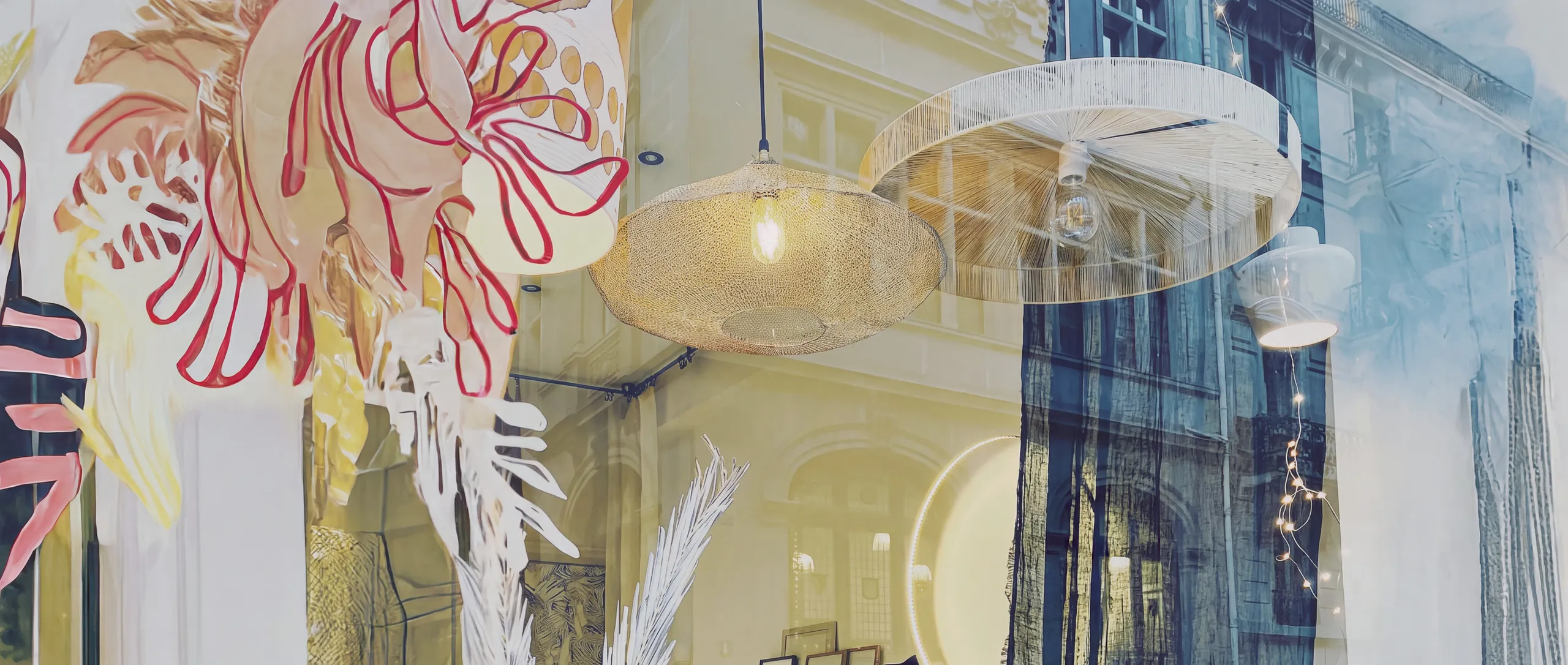 La vitrine de la boutique : suspensions en maille dorée et en fils blancs, avec le reflet de la rue