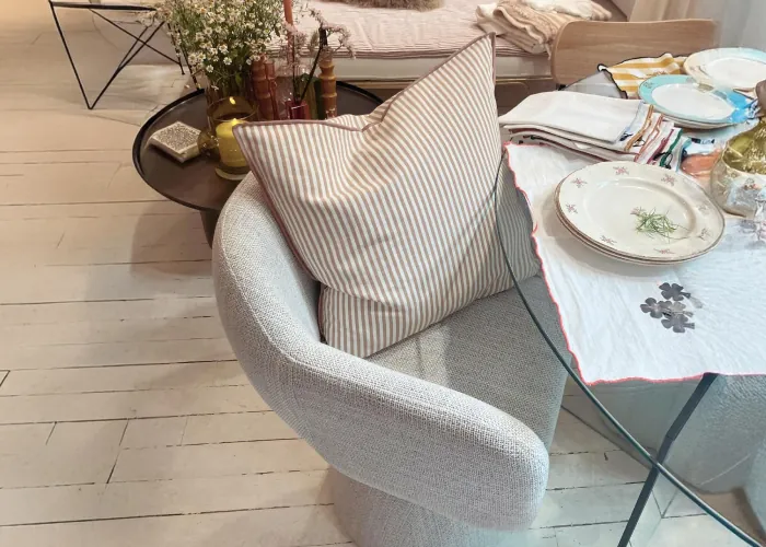 Fauteuil gris en tissu bouclé avec un coussin rayé, près d'une table en verre dressée