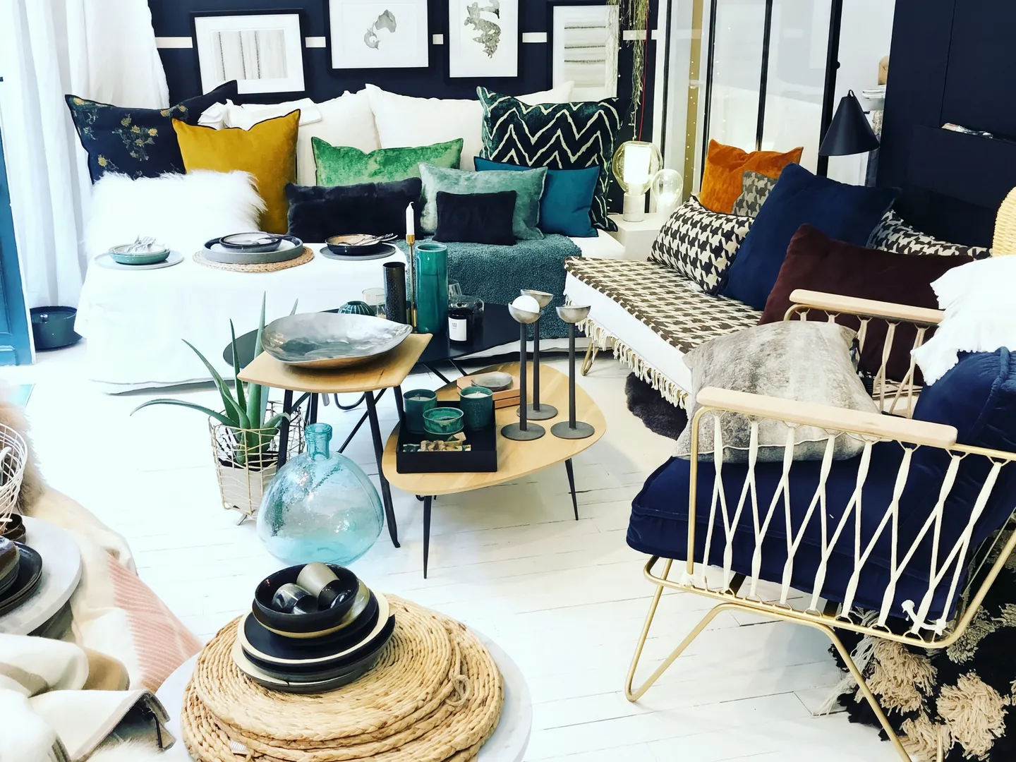Un coin salon de la boutique : canapé garni de coussins, tables basses gigognes et fauteuil en métal doré