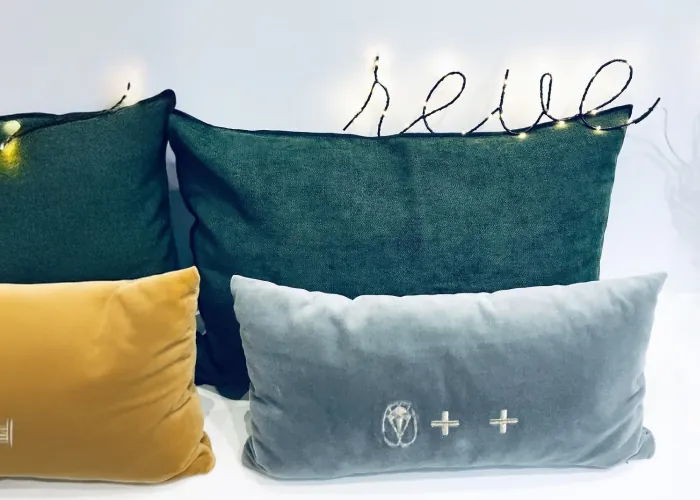 Coussins en velours vert, moutarde et gris sous une guirlande lumineuse « rêve »