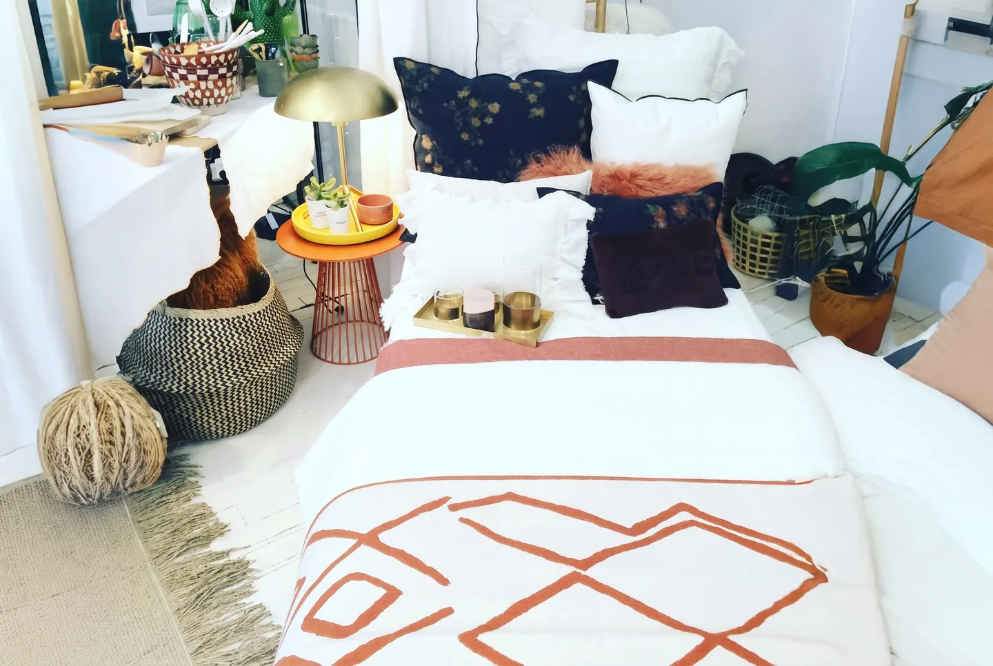 Lit habillé d'un plaid blanc à motifs rouille et de coussins